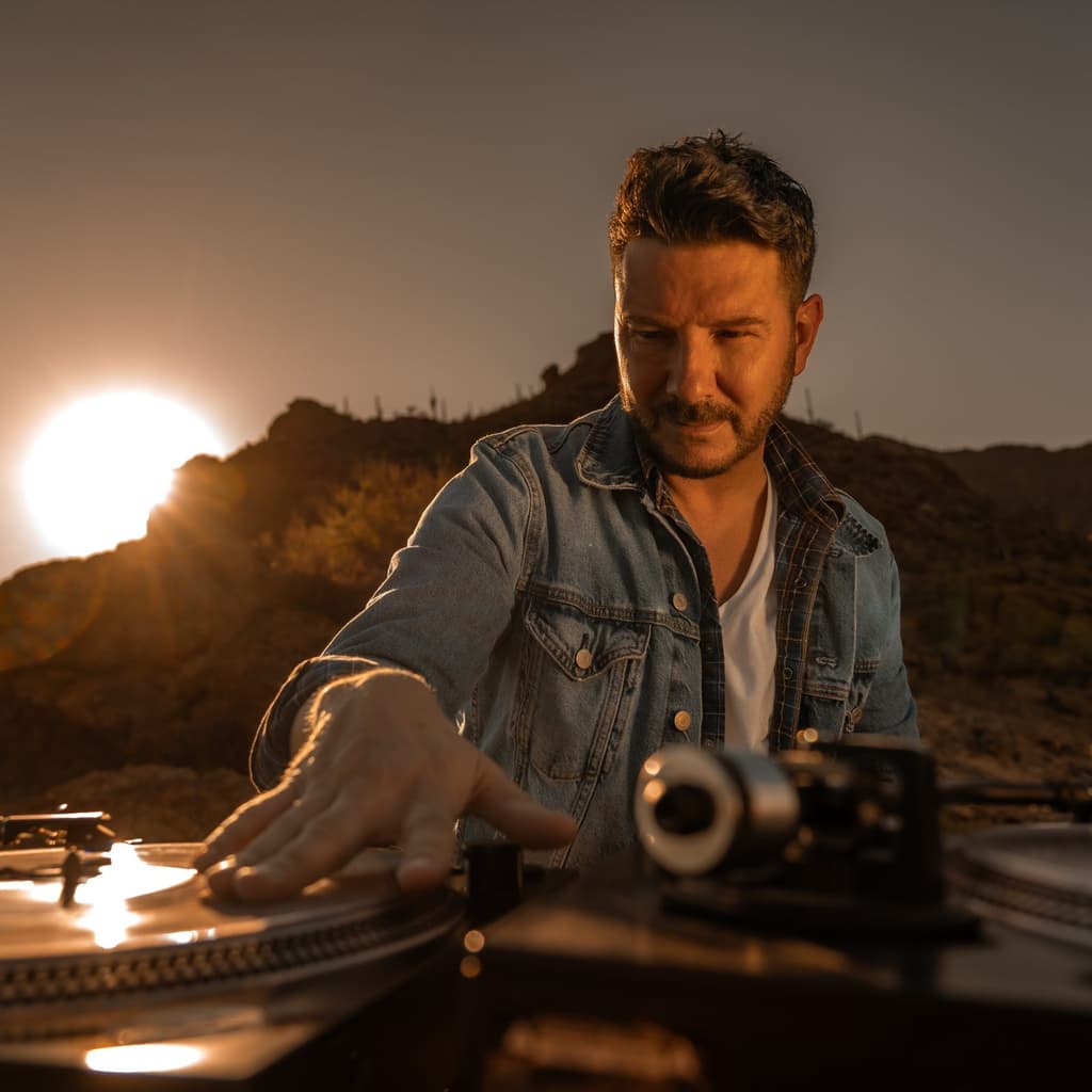 DJ Du with a DJ equipment in the desert with the sunseting in the mountain